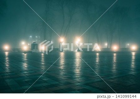 Alley of a night winter park in a fog. Footpath in a fabulous winter city park at night in fog with benches and latterns. Beautiful foggy evening in the Mariinsky Park. Kyiv, Ukraine. Alley of a night winter park in a fog. Footpath in a fabulous winter city park at night in fog with benches and latterns. Beautiful foggy evening in the Mariinsky Park. Kyiv, Ukraine. 141099144