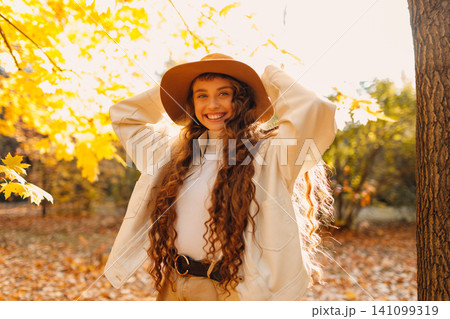 Smiling young woman in the autumn forest with the yellow leaves with sunset rays Smiling young woman in the autumn forest with the yellow leaves with sunset rays 141099319