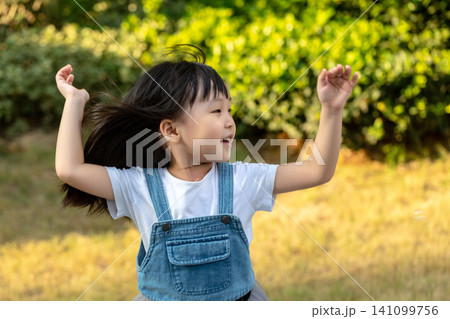 Energetic little Asian girl tossing her hair while playing outdoors in sunlight Energetic little Asian girl tossing her hair while playing outdoors in sunlight 141099756