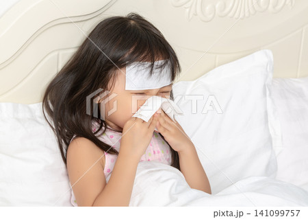 Asian Little Girl Blowing Nose with Tissue While Sick in Bed Asian Little Girl Blowing Nose with Tissue While Sick in Bed 141099757