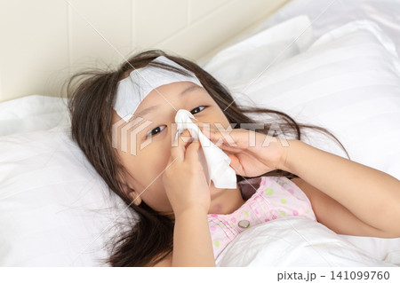 Asian Little Girl Blowing Nose with Tissue While Sick in Bed Asian Little Girl Blowing Nose with Tissue While Sick in Bed 141099760