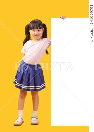 Full length view of a smiling school girl standing next to a large vertical blank white display board on a bright yellow backdrop. Full length view of a smiling school girl standing next to a large vertical blank white display board on a bright yellow backdrop. 141099791