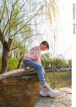 A young girl climbing on a rustic stone wall at an outdoor park. A young girl climbing on a rustic stone wall at an outdoor park. 141099939