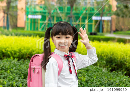 Asian elementary school students carrying their schoolbags happily walk in the city park after school. Asian elementary school students carrying their schoolbags happily walk in the city park after school. 141099980