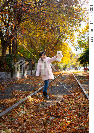 A happy child walking on an old railway track while raising her white teddy bear to show joy. A happy child walking on an old railway track while raising her white teddy bear to show joy. 141100001