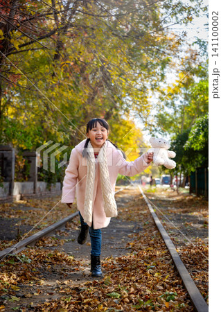 A happy child walking on an old railway track while raising her white teddy bear to show joy. A happy child walking on an old railway track while raising her white teddy bear to show joy. 141100002