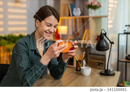 Young woman on home table playing smartphone game winning happy celebrating victory at home indoors Young woman on home table playing smartphone game winning happy celebrating victory at home indoors 141100081