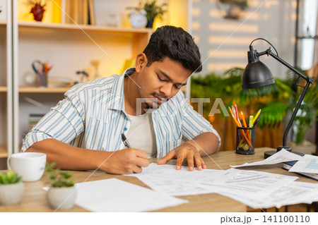 Indian man on home table reading final line on paper before signing office document before approval Indian man on home table reading final line on paper before signing office document before approval 141100110