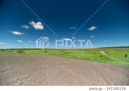 Sunny rural landscape with gravel foreground and green fields under blue sky Sunny rural landscape with gravel foreground and green fields under blue sky 141100138