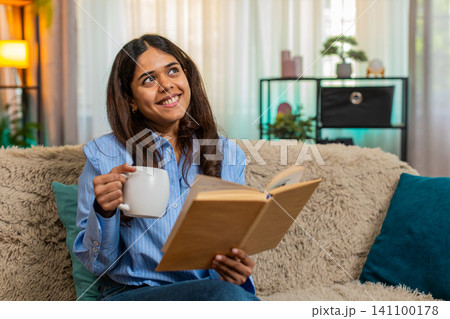 Indian woman drinking coffee and reading book at home enjoying quiet peaceful start of cozy morning Indian woman drinking coffee and reading book at home enjoying quiet peaceful start of cozy morning 141100178