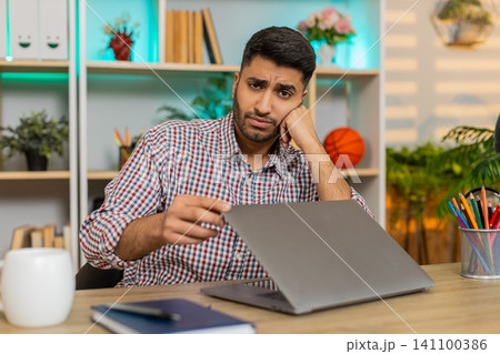 Indian man on home table frustrated by laptop closing work after failure during remote job indoors 141100386