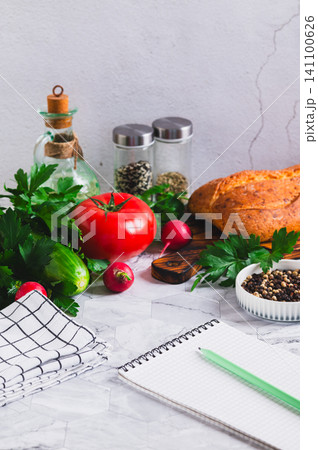Open recipe notebook, vegetables, herbs and bread on the kitchen table vertical view Open recipe notebook, vegetables, herbs and bread on the kitchen table vertical view 141100626