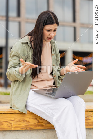 Young woman receiving bad news walking in city street feeling upset with laptop and closing screen 141100825