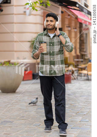 Indian man listening to music walking in city street with wireless headphones smiling during stroll Indian man listening to music walking in city street with wireless headphones smiling during stroll 141100838