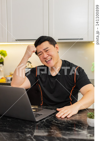 Upset Asian man reacts to bad online casino loss while reading laptop screen at home kitchen indoors Upset Asian man reacts to bad online casino loss while reading laptop screen at home kitchen indoors 141100899