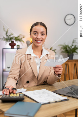Young businesswoman totals month on calculator checks receipts and invoices nods with satisfaction Young businesswoman totals month on calculator checks receipts and invoices nods with satisfaction 141100997