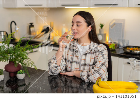 Young woman drinks filtered water in kitchen, healthy habit hydration routine and wellness lifestyle Young woman drinks filtered water in kitchen, healthy habit hydration routine and wellness lifestyle 141101051