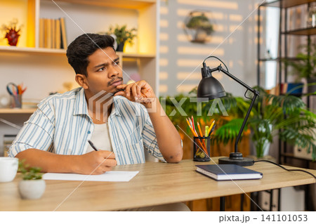 Indian man on home table writing shopping list on paper and planning home purchases with calm focus Indian man on home table writing shopping list on paper and planning home purchases with calm focus 141101053