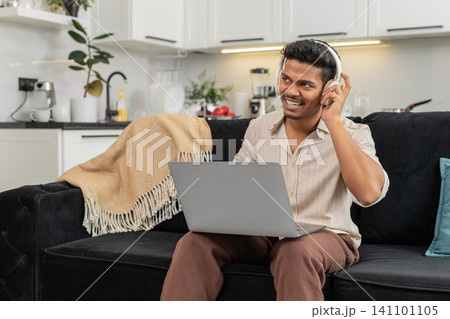 Indian man with wireless headphones edits short video on laptop works freelance smiles with approval Indian man with wireless headphones edits short video on laptop works freelance smiles with approval 141101105