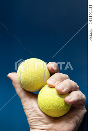 Hand holding two yellow tennis balls on a blue background. Hand holding two yellow tennis balls on a blue background. 141101131