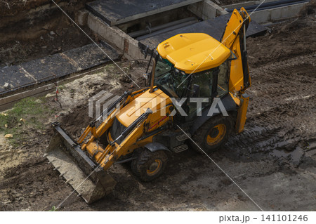 Yellow backhoe loader at muddy construction site near concrete pipes. Yellow backhoe loader at muddy construction site near concrete pipes. 141101246