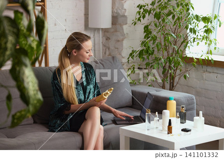Woman choosing beauty products with laptop in plant filled living room. 141101332