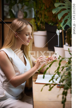 Woman examining skincare serum while taking beauty notes at desk. Woman examining skincare serum while taking beauty notes at desk. 141101350