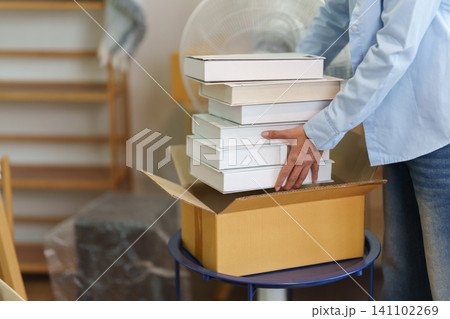 Cropped person packing stack of books into cardboard box for moving 141102269