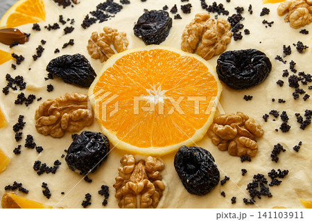 Orange slice with walnuts, prunes and poppy seeds on cake, close-up 141103911