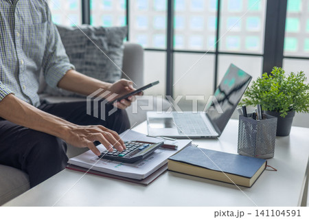 Businessman calculating expenses and reviewing financial statistics on phone and laptop. 141104591
