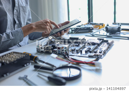 IT technician using tablet while repairing laptop motherboard and computer hardware components. IT technician using tablet while repairing laptop motherboard and computer hardware components. 141104897