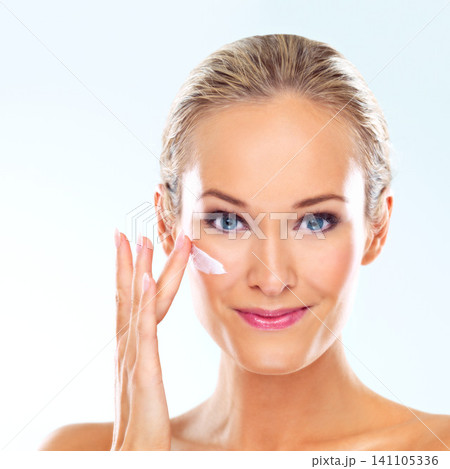 Woman, studio and portrait with cream on face for skincare, dermatology, and self care with smile. Female person, happy and facial product with lotion, cosmetics or beauty glow on blue background Woman, studio and portrait with cream on face for skincare, dermatology, and self care with smile. Female person, happy and facial product with lotion, cosmetics or beauty glow on blue background 141105336
