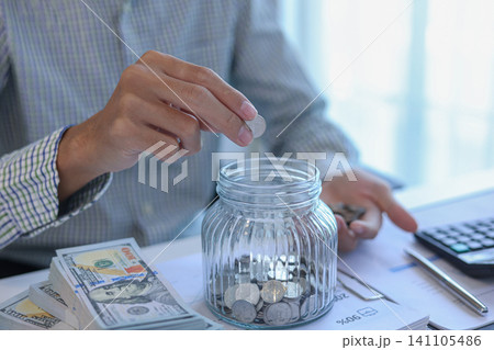 Saving Money Concept. Businessman Putting Coins into Glass Jar Smart Money Habits and Financial Literacy Visual 141105486