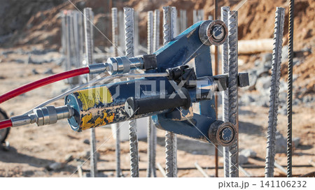 A machine is used to bend reinforcement bars for foundations at a construction site. Workers prepare materials on the ground for the bending process A machine is used to bend reinforcement bars for foundations at a construction site. Workers prepare materials on the ground for the bending process 141106232