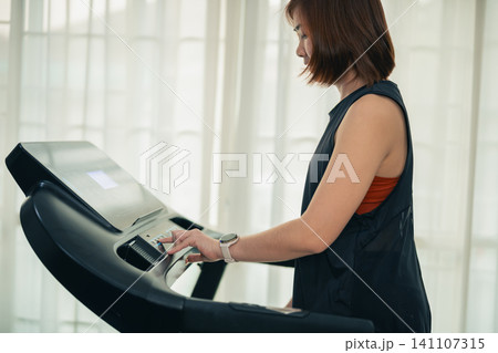 Young woman adjusting treadmill settings during indoor workout at home gym Young woman adjusting treadmill settings during indoor workout at home gym 141107315