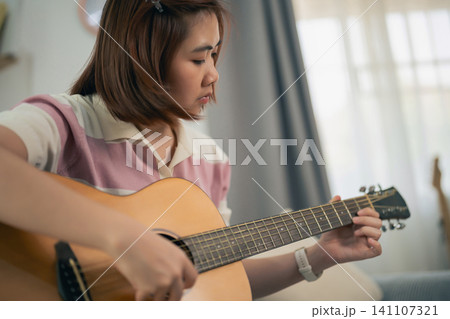 Young woman focused on playing acoustic guitar indoors in natural light Young woman focused on playing acoustic guitar indoors in natural light 141107321