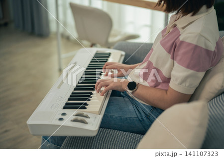 Young woman playing electronic keyboard while sitting on sofa at home Young woman playing electronic keyboard while sitting on sofa at home 141107323