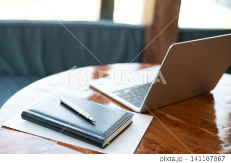 Notebook with pen beside laptop on wooden table in cafe Notebook with pen beside laptop on wooden table in cafe 141107867