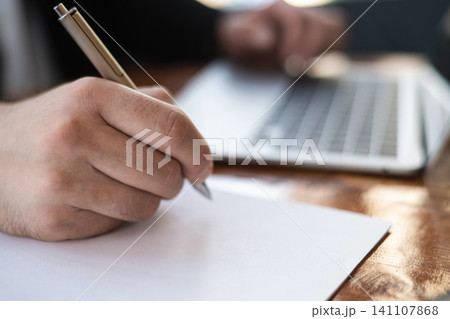 Close up of businessman writing notes while working on laptop computer Close up of businessman writing notes while working on laptop computer 141107868
