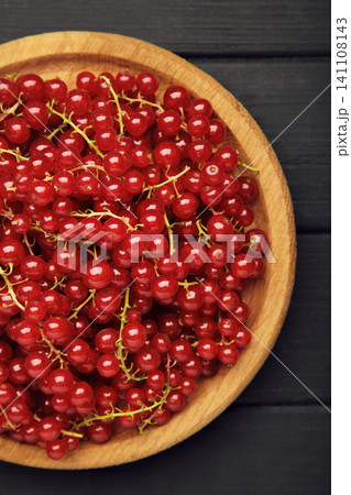 Red currants on wooden plate on black wooden background. Fresh and vibrant food photography for healthy eating. Vertical photo Red currants on wooden plate on black wooden background. Fresh and vibrant food photography for healthy eating. Vertical photo 141108143