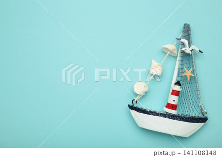 Decorative sailboat ornament with striped lighthouse detail, fabric sail, seashell garland on blue background. Summer concept Decorative sailboat ornament with striped lighthouse detail, fabric sail, seashell garland on blue background. Summer concept 141108148