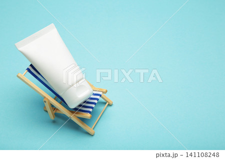 Cosmetic facial cream in plastic tube on miniature deck chair on blue background. Summer concept. 141108248