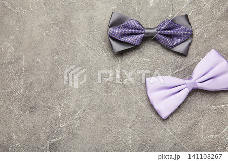 Two elegant grey and purple bow tie on grey concrete background. Two elegant grey and purple bow tie on grey concrete background. 141108267