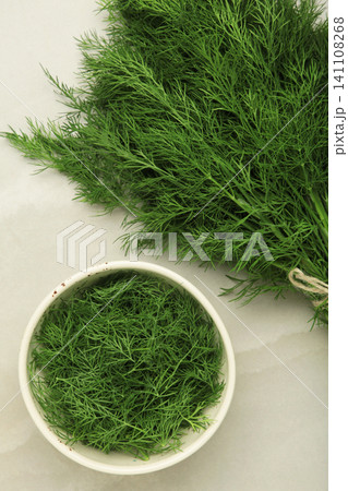 Bunch of green dill and dill on white bowl on grey background. Bunch of green dill and dill on white bowl on grey background. 141108268