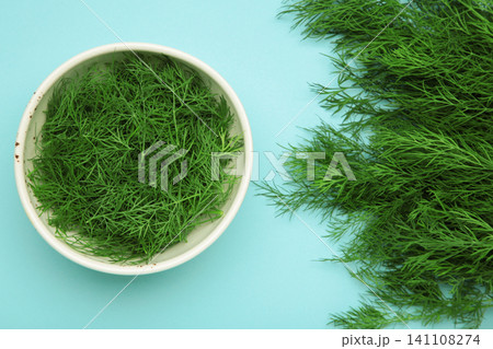 Bunch of green dill and dill on white bowl on blue background. Bunch of green dill and dill on white bowl on blue background. 141108274