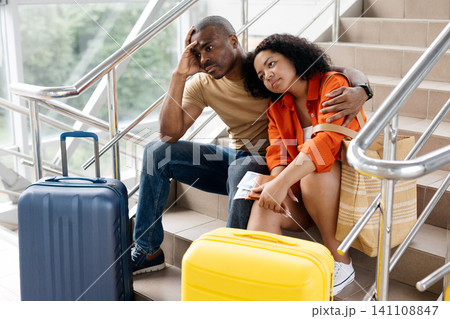 Bored black couple embracing on airport stairs, holding tickets, waiting patiently 141108847