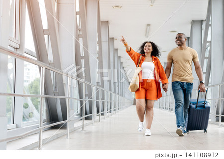 Black woman pointing excitedly while walking with partner through airport corridor Black woman pointing excitedly while walking with partner through airport corridor 141108912