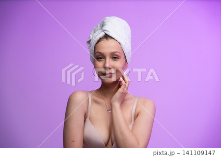 Woman wearing towel turban after shower, touching her clean skin, promoting beauty, skincare, wellness, and self-care on a purple background with copy space Woman wearing towel turban after shower, touching her clean skin, promoting beauty, skincare, wellness, and self-care on a purple background with copy space 141109147