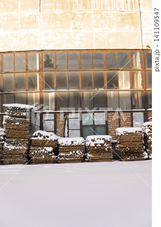 Wooden pallets covered in snow outside an abandoned factory building with large industrial windows in winter Wooden pallets covered in snow outside an abandoned factory building with large industrial windows in winter 141109547