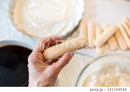 Woman hand holding ladyfinger biscuit over coffee dessert preparation 141109548